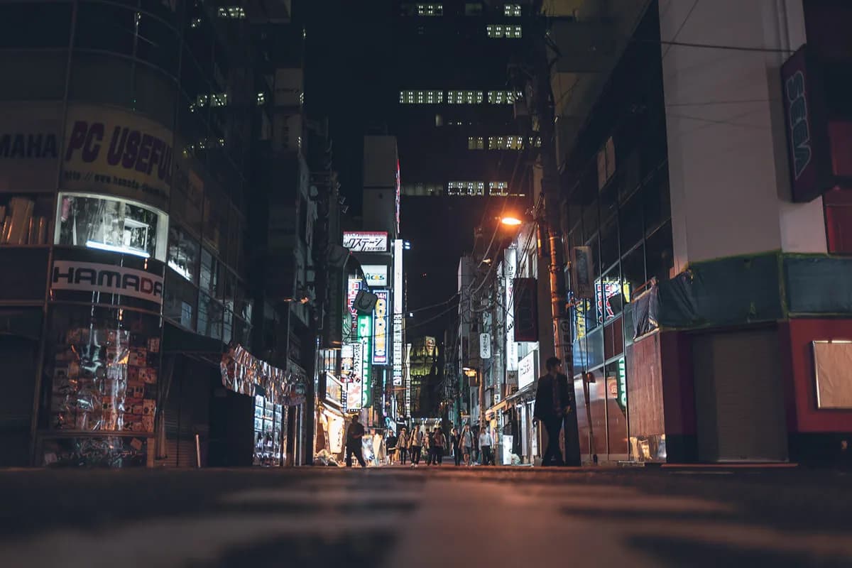 Low-angle night photo of a Tokyo shopping street, neon signs fading into the distance between dark buildings.